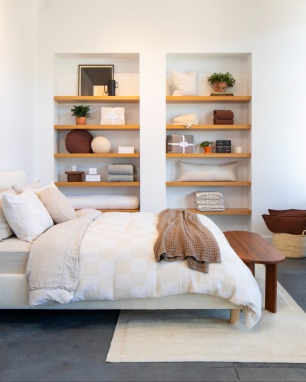 Side view of a neat bed next to shelves filled with assorted bedding products