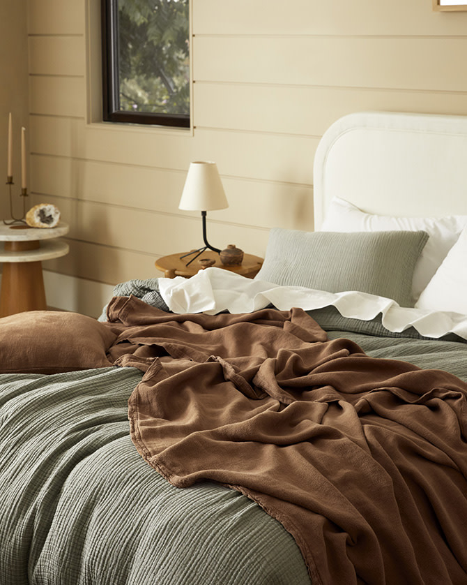 A messy bed with moss green and pecan brown bedding