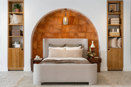 A neatly made bed under an archway with terracotta tiles