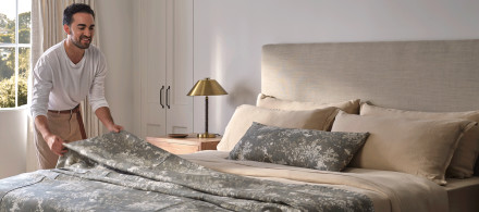 Celebrity designer Jake Arnold placing a sage botanical print bedspread on a neatly made bed
