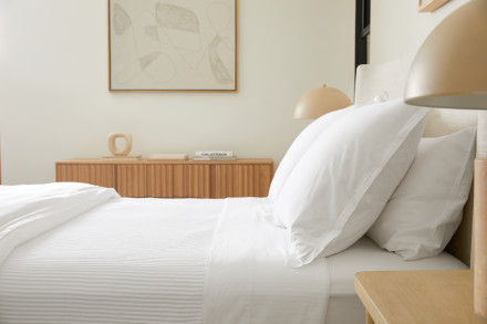 Side angle of bed dressed in white percale sheeting