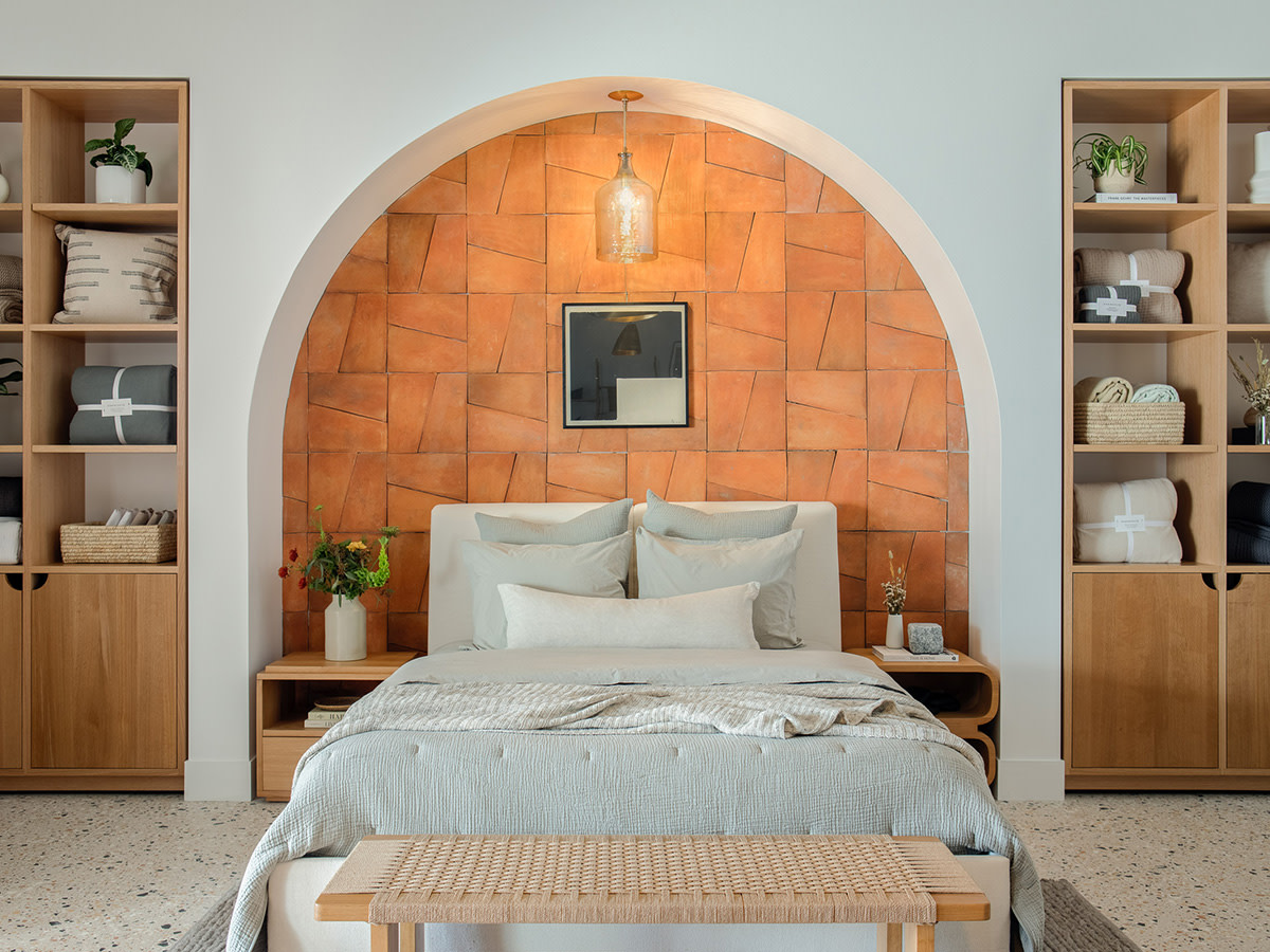 A neatly made bed sitting in a terracotta tile archway in a spacious showroom.