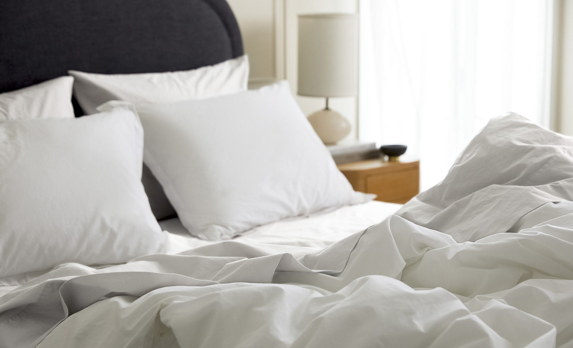 Close up of a messy bed with white and light grey sheets