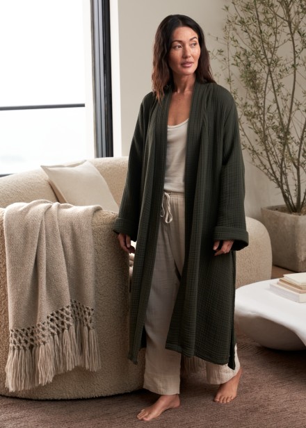 A person wearing a dark hunter green cotton gauze robe and walking through a living room