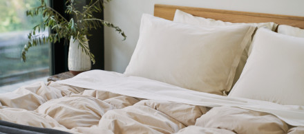 A bed with white sheets and a bone organic cotton puff comforter