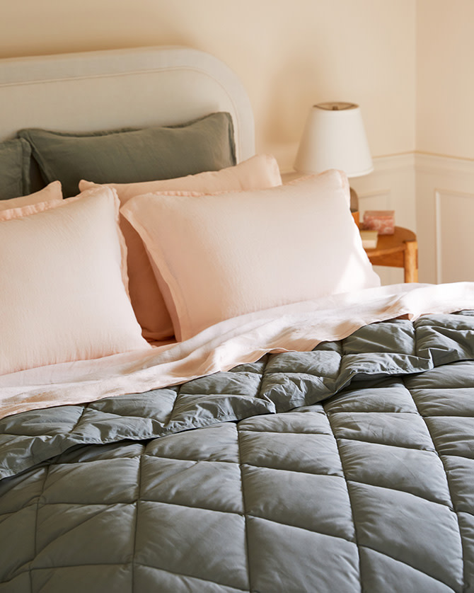 Light pink linen sheets under a moss green puffy comforter
