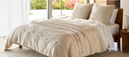 A bed with an ivory linen quilt and white sheets