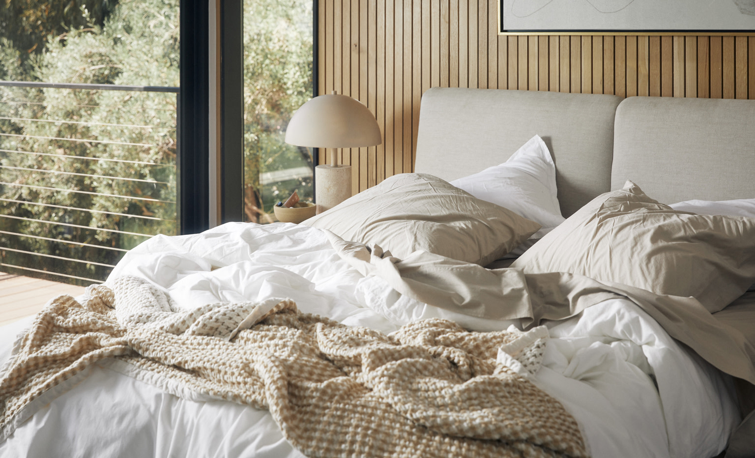 Messy bed featuring white percale sheeting and a natural colored throw