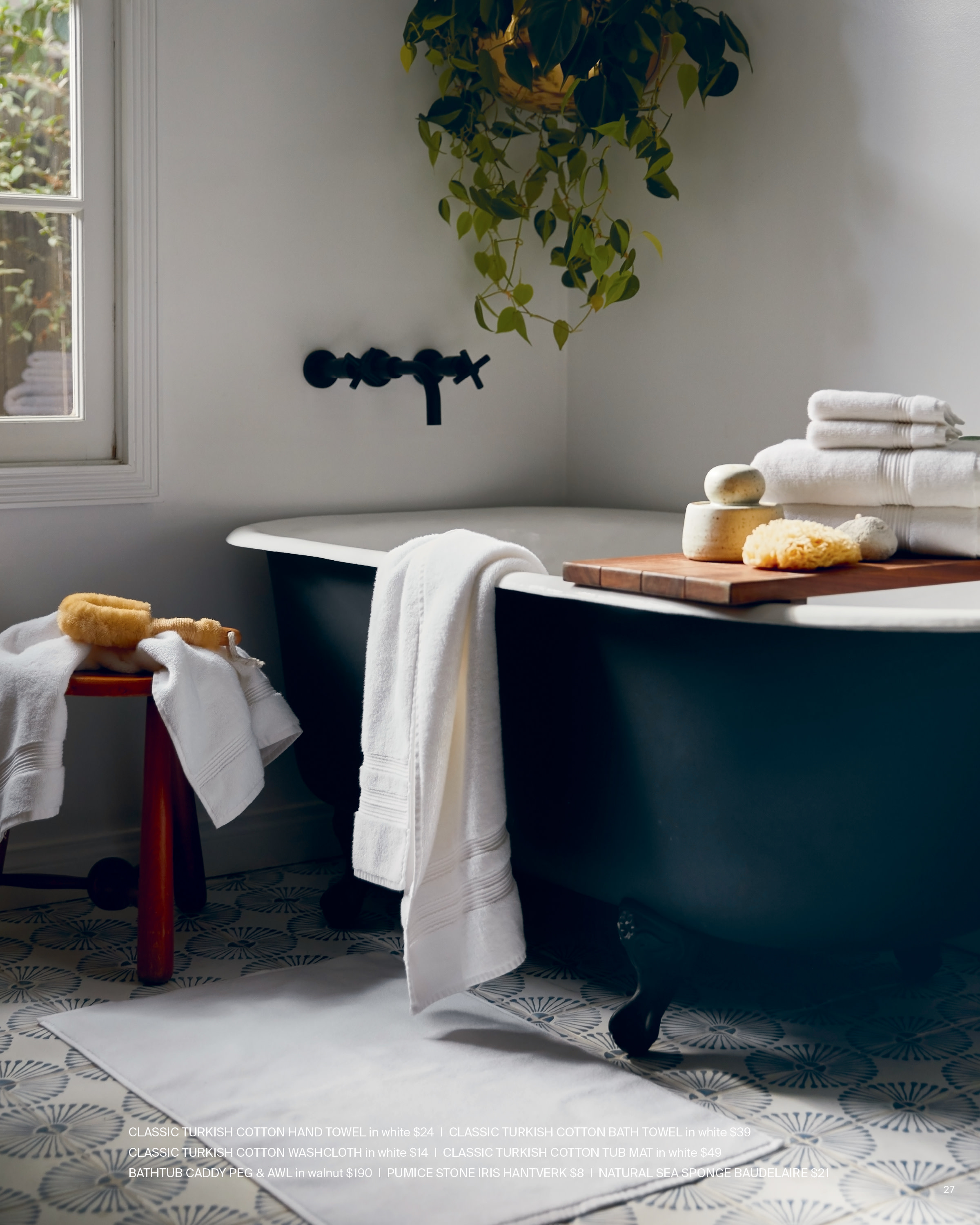 A black bathtub with a set of white towels in a naturally lit bathroom.