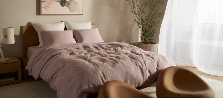 A bed with dusty greyish purple linen sheets