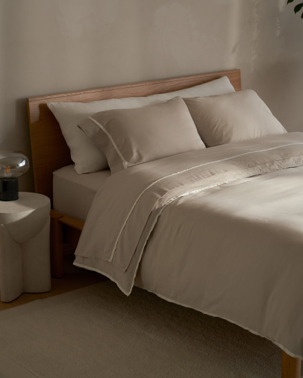 A neatly made bed with bone organic soft luxe sheets with cream piping