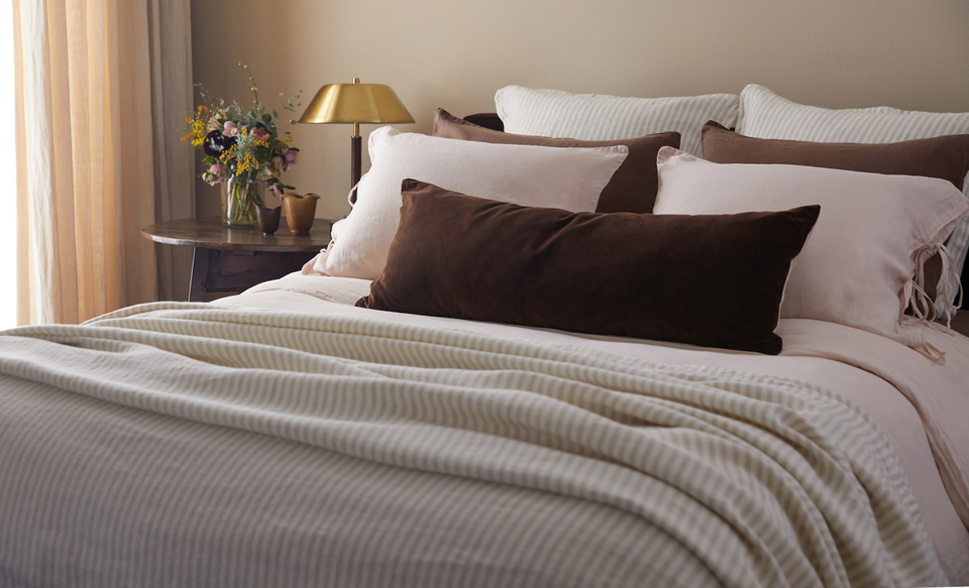 Close up image of a made bed with white sheets and a brown velvet pillow.