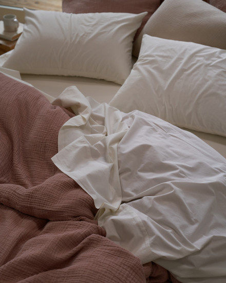 A messy bed with white cotton sheets and a clay cloud cotton duvet cover