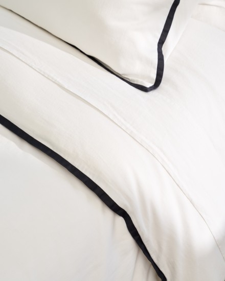A close-up view of a Organic Soft Luxe bed in white with soft black piping