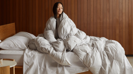 Person wrapped in a puff comforter sitting on a comfy looking bed