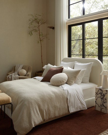 A bed with a textured duvet cover and multiple decorative pillows in natural tones of white and beige