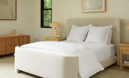 A neatly made bed with white sheets in a bright sunny bedroom