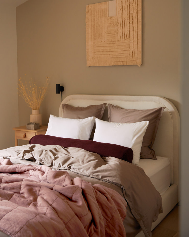 Image of a Parachute bed frame layered with pillows and blankets in warm pink, red, and white color tones.