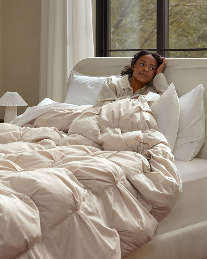 A woman sitting in a cozy bed with a puffy comforter