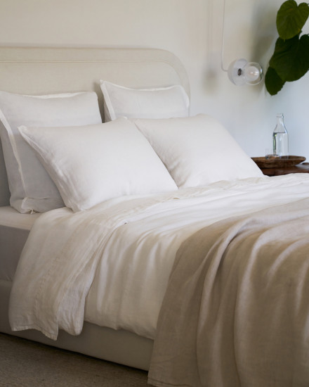 A bed with white linen sheets and a bone linen quilt