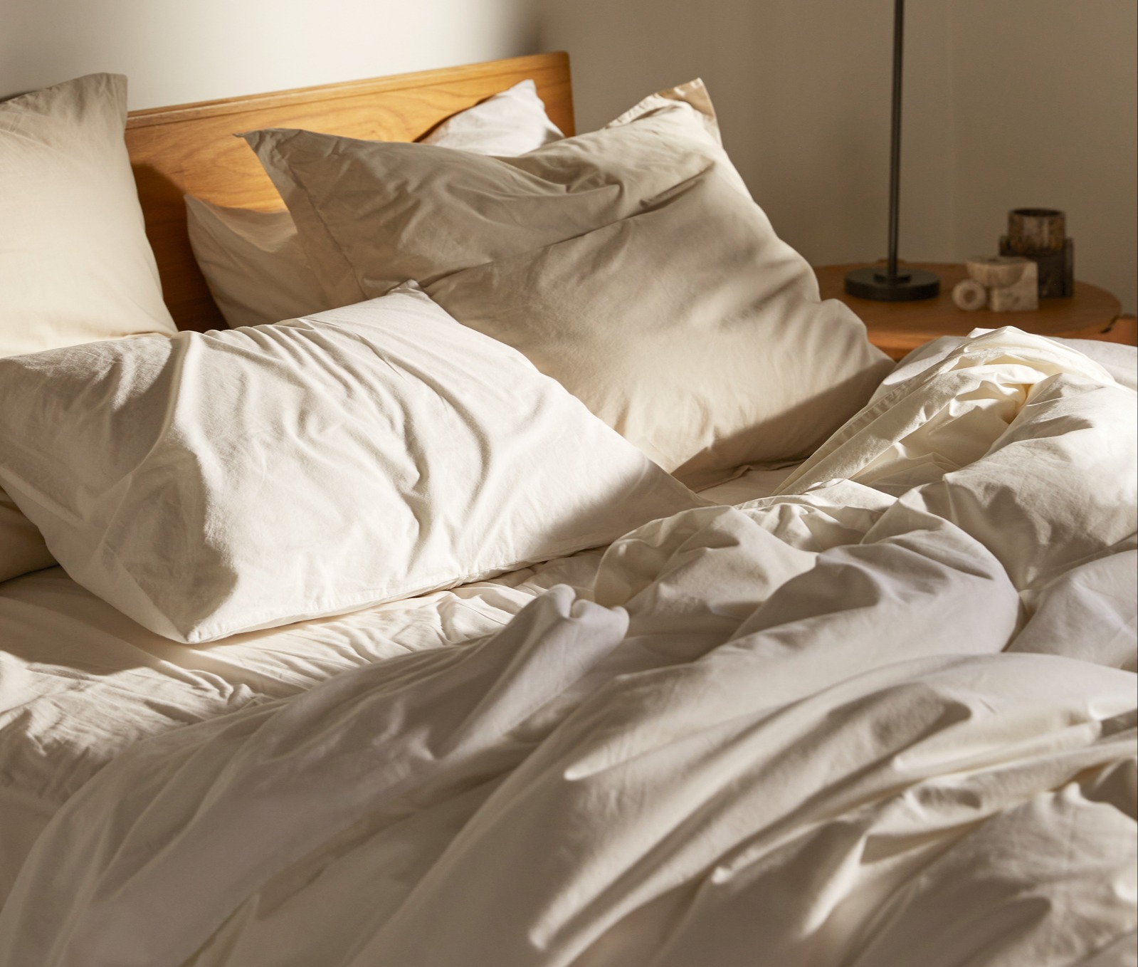 A messy bed with white and tan organic cotton sheets