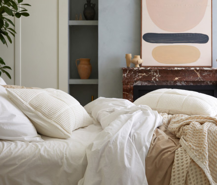 A messy bed with white and tan organic cotton sheets