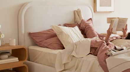 A person reading in a bed with cream and clay percale sheets