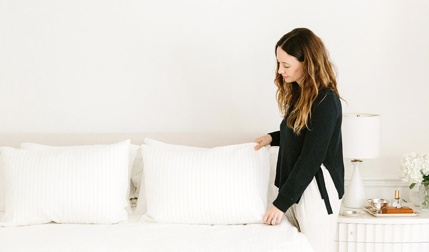 Jenni Kayne fixing pillows on a bed. 