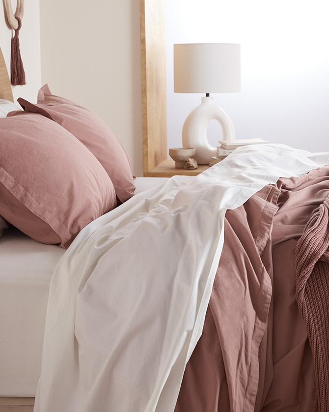 A bed with white and clay pink percale sheets