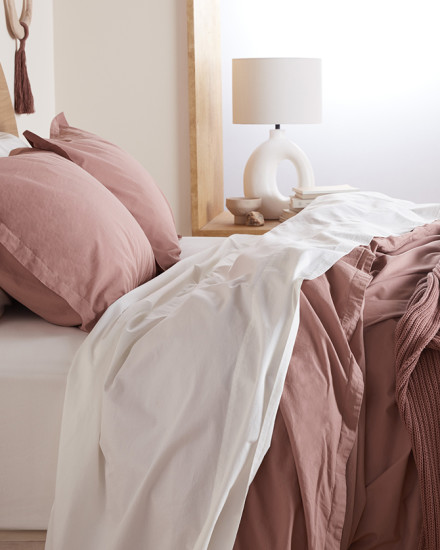 A bed with white and clay pink percale sheets