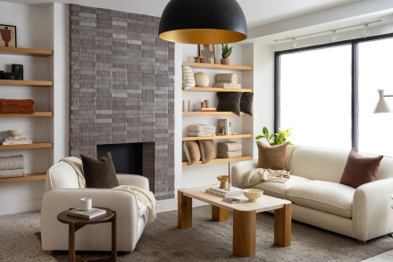 A bright seating area with a plush ivory sofa and chair, in front of a grey-tiled fireplace