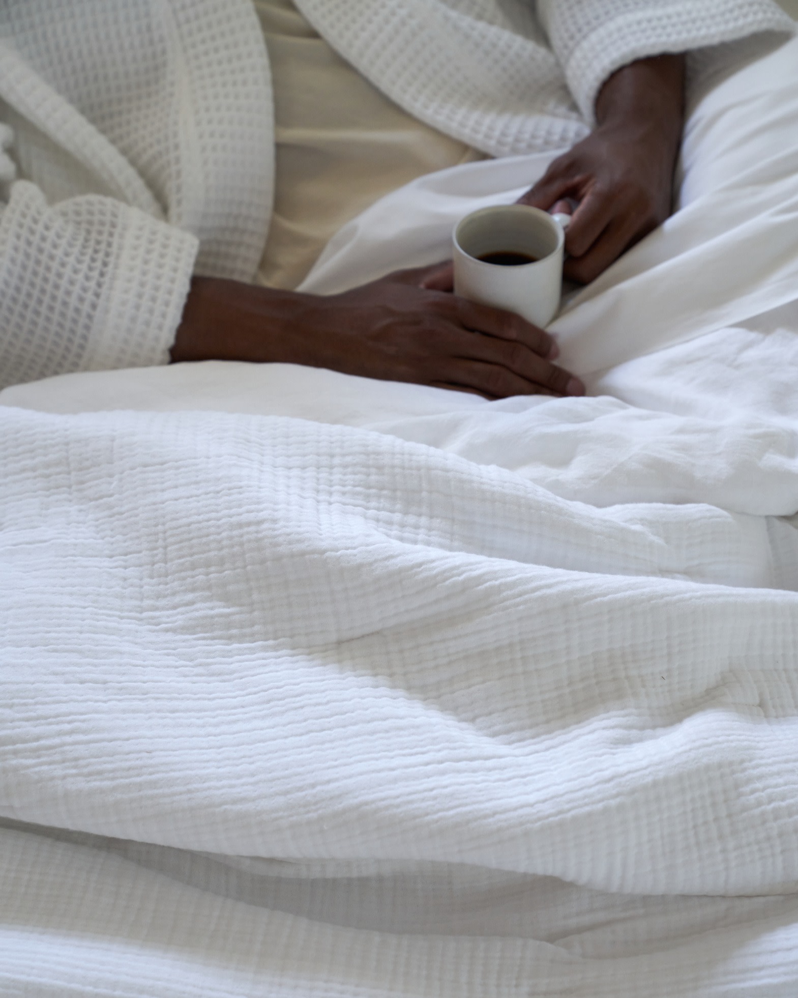 A person drinking coffee in a cozy bed with plush white bedding