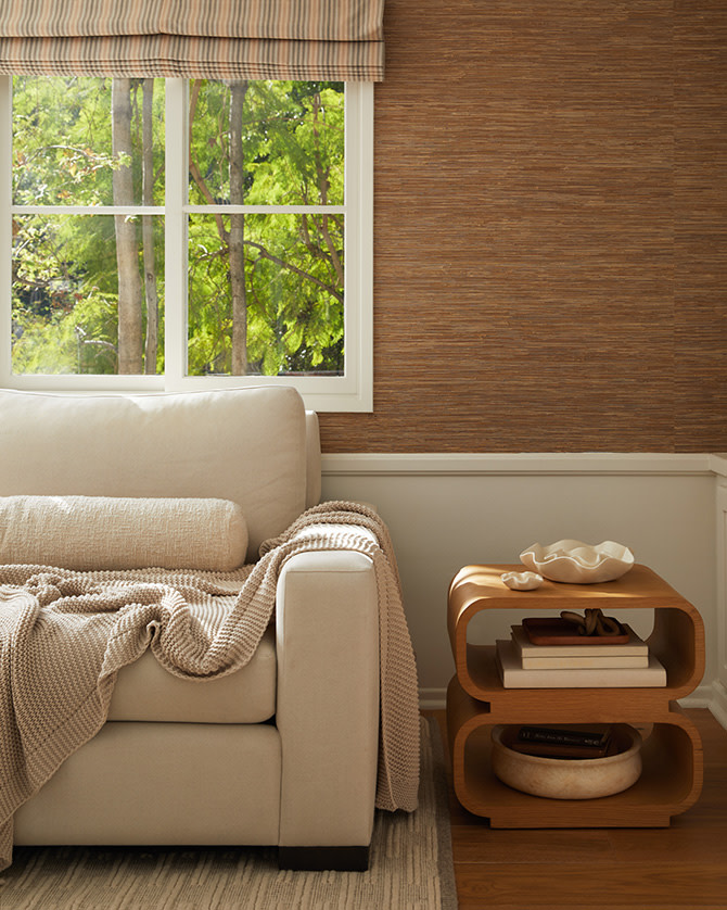 A beige sofa with a knit blanket and boucle pillow next to an oval wood side table.