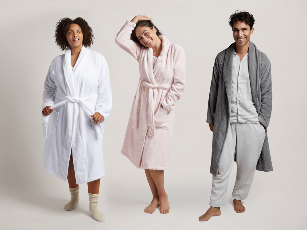 Two women and a man standing next to each other in classic bathrobes.