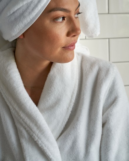 A person wearing a plush white robe and sitting on the edge of a marble tub