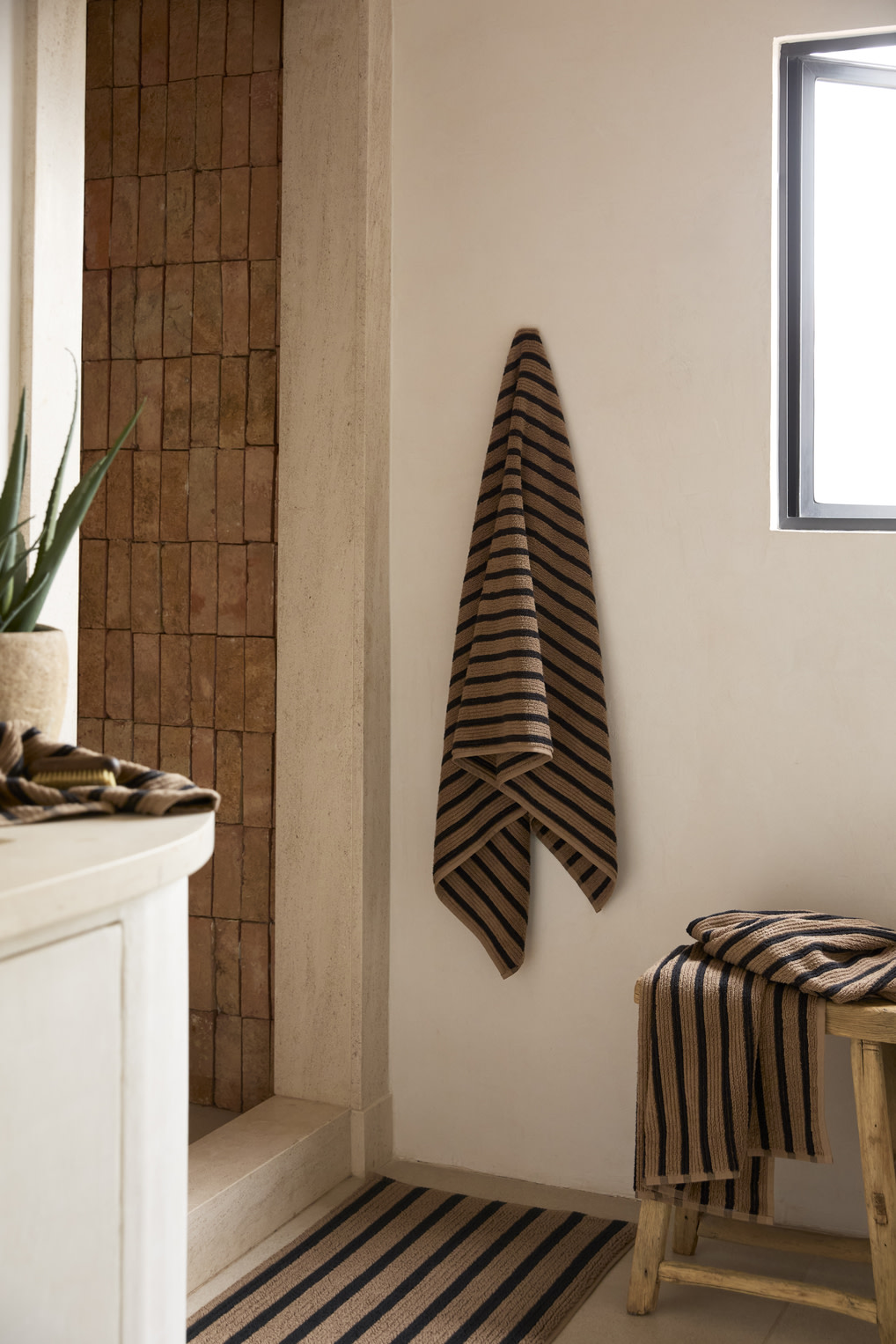 Camel and black resort stripe towels and tub mat in a bathroom