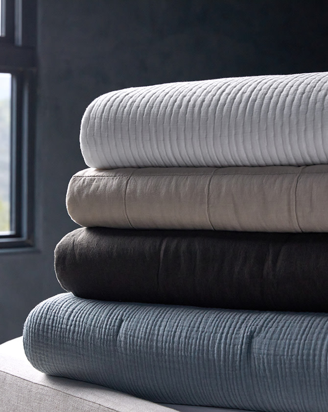 A stack of plush quilts in white, ivory, dark grey, and calm blue