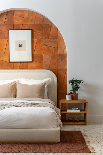 A neatly made bed against an archway with terracotta tiles