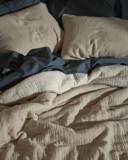 A bed with dusk blue sheets and a beige cloud cotton quilt and shams