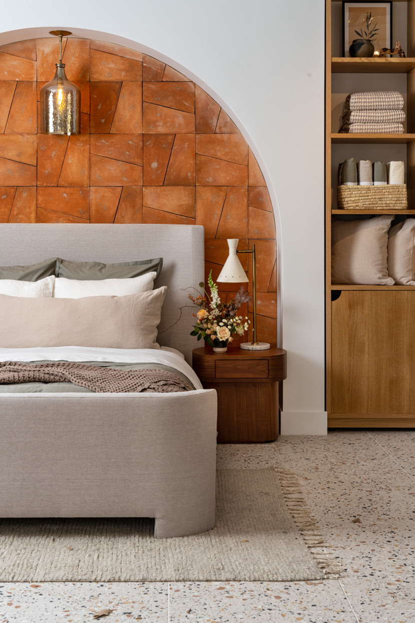 A neatly made bed under an archway made with terracotta tiles