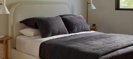A curved ivory bed frame with dark grey linen sheets