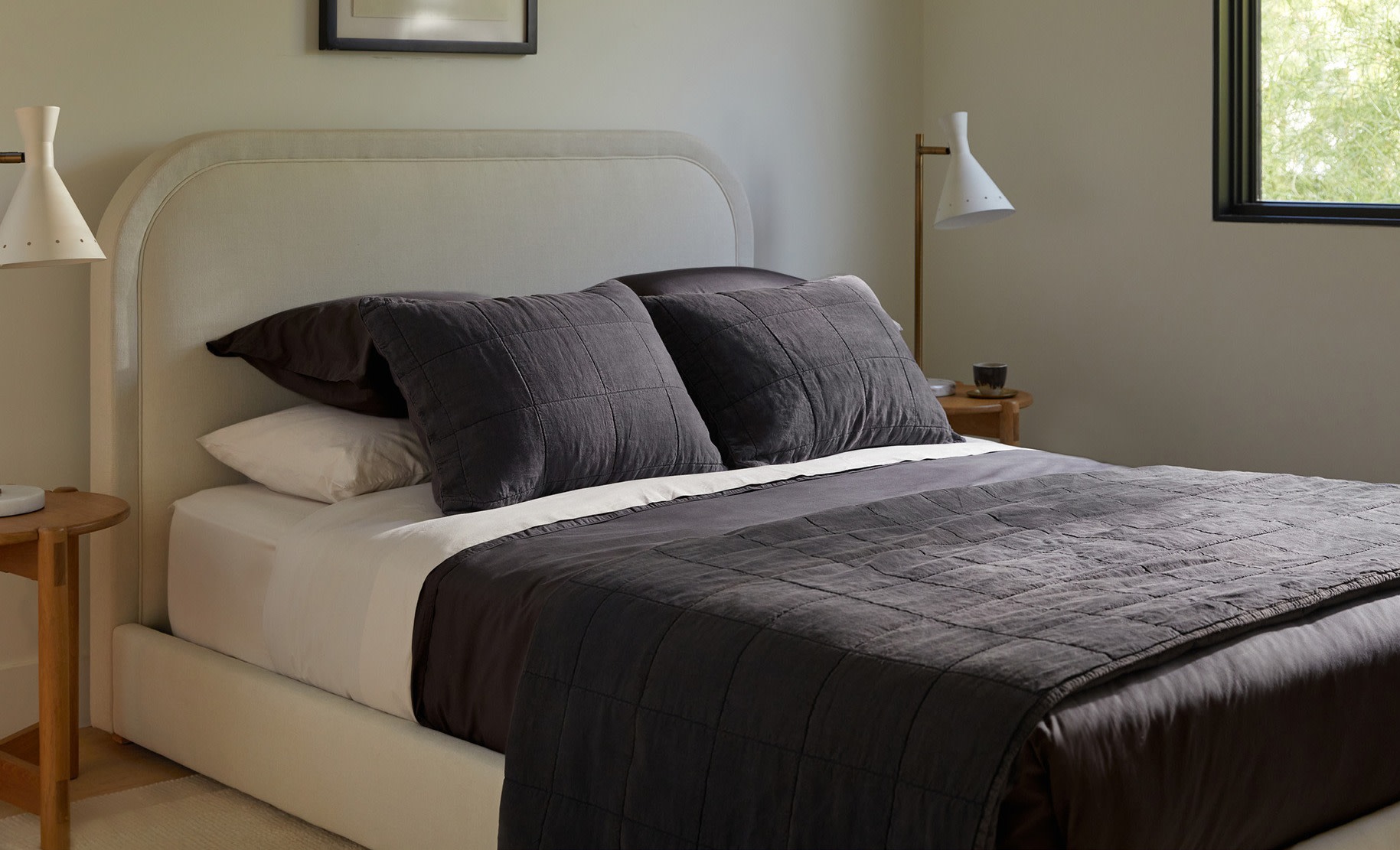 A curved bed frame with dark grey linen sheets