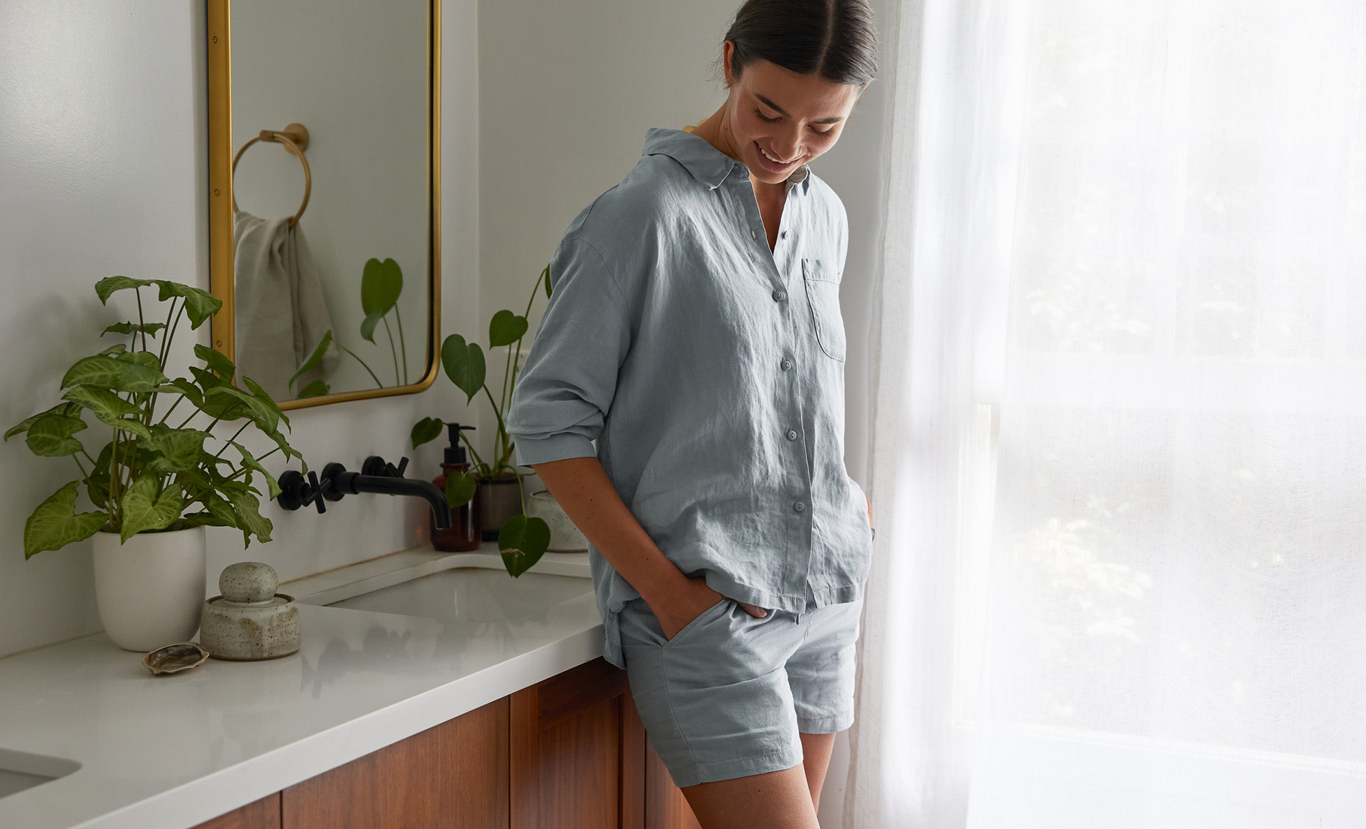 Woman in slate blue linen loungewear leaning against a bathroom counter
