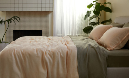 Side view of a bed with light pink and moss green linen sheets