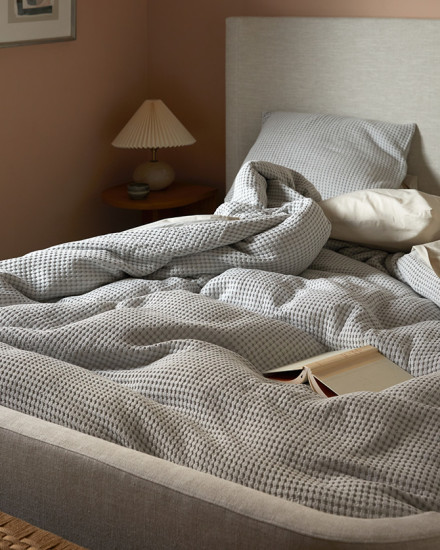 A messy bed with a light grey waffle duvet cover