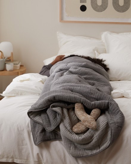 A person wrapped in a cozy grey quilt with their feet sticking out of the bottom
