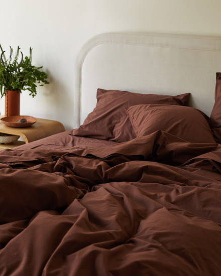 An unmade bed with raisin percale sheets.