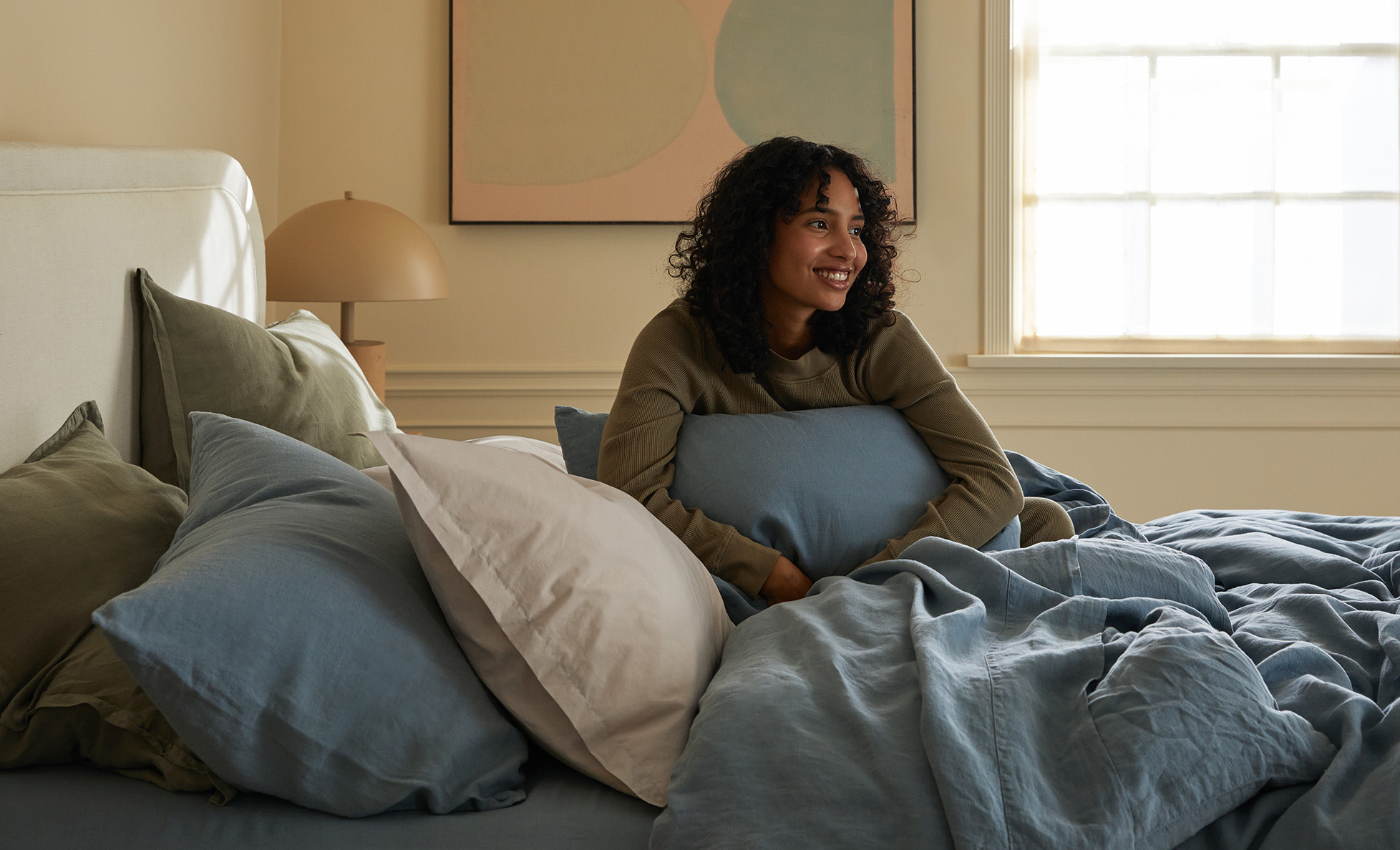 A woman hugging a pillow in a bed of blue and green sheets