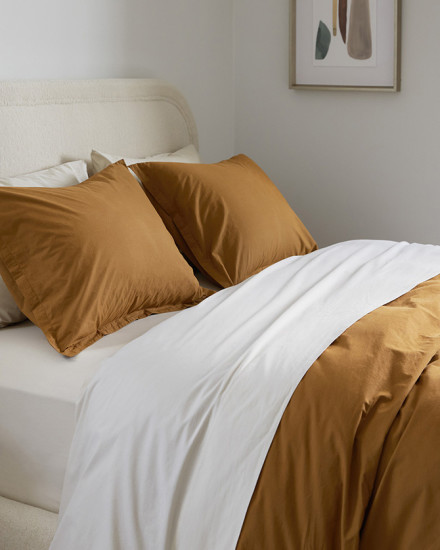 A neat bed with white and ochre yellow brushed cotton sheets
