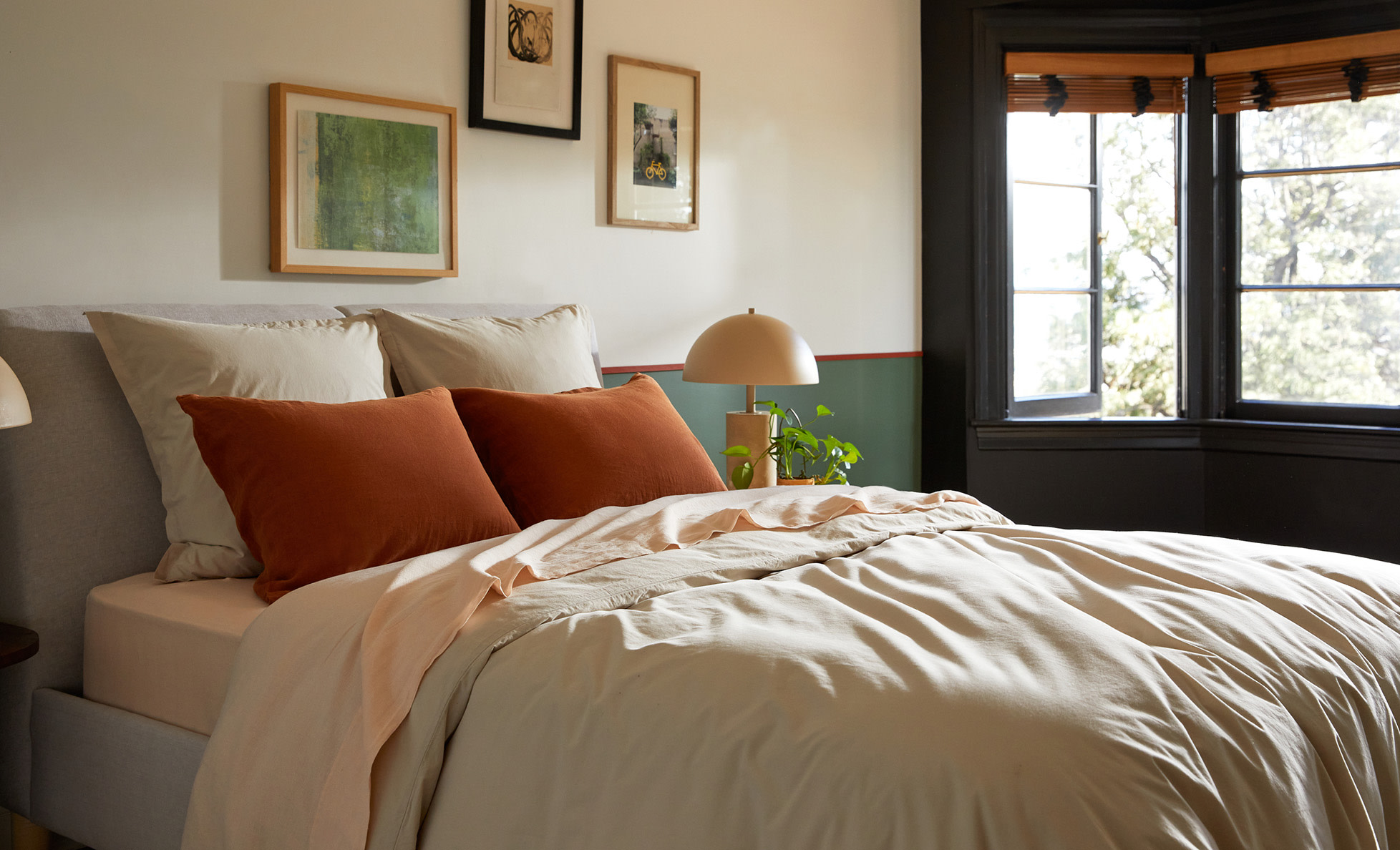 A casual bed with neutral toned sheeting and orange pillows